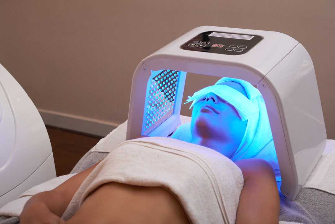 A person receiving a Skinwave Facial under a blue LED therapy device in a spa setting.